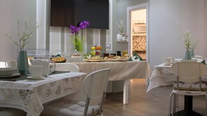 A modern dining area with a flat-screen TV mounted on the wall, a buffet table with various food items, and a seating arrangement with chairs and tables. - 360 Hospitality (Salerno)