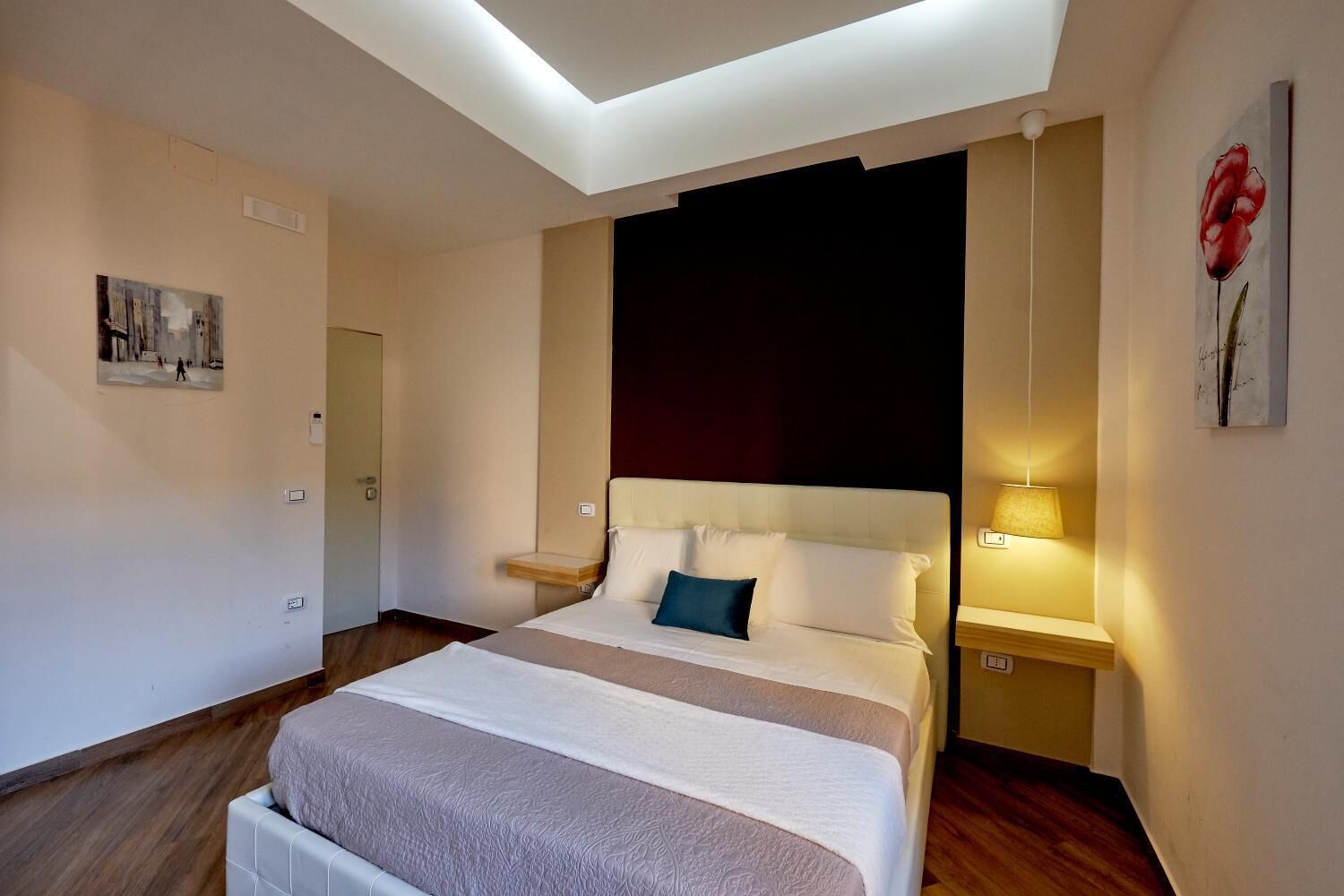 A modern hotel room with a large bed, bedside tables, a ceiling light, and a painting on the wall.