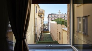A narrow alleyway with buildings on either side, a green lawn, and a cross on a building in the distance. - 360 Hospitality (Salerno)