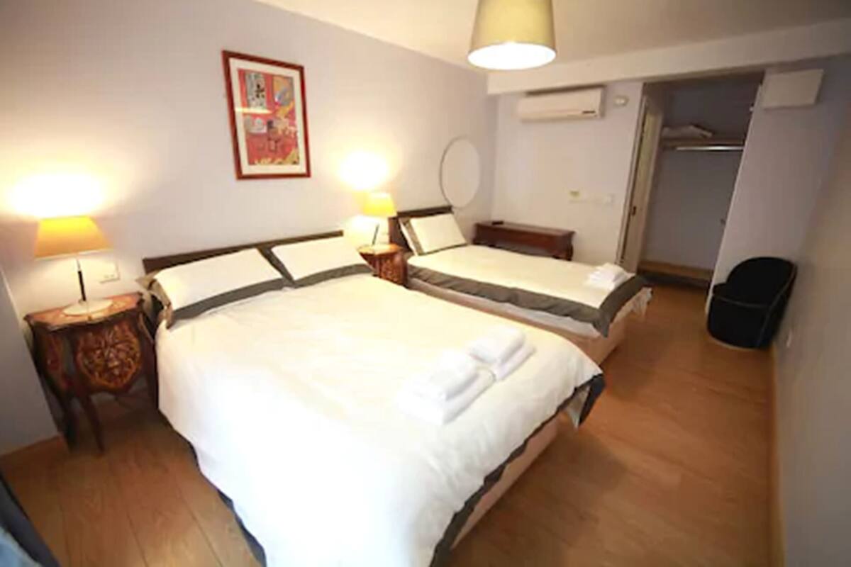 A hotel room with two single beds, a bedside table with a lamp, a wardrobe, and a trash bin.