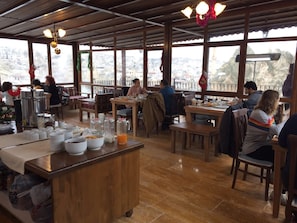 A restaurant with wooden tables and chairs, a counter with food and drink containers, and large windows offering a view of the city.