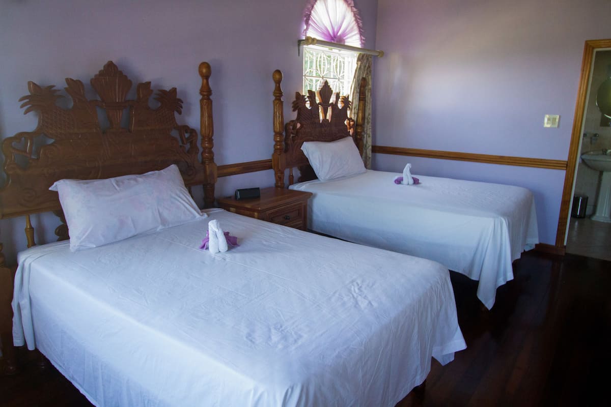 A hotel room with two single beds, a wooden headboard, a nightstand, and a window with a curtain.