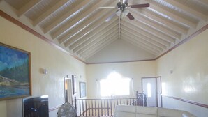A spacious living room with a high ceiling, a ceiling fan, a large white leather sofa, a flat-screen TV, and a wooden coffee table. - Steel Love Villa (Montego Bay)