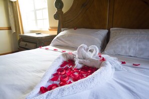 A neatly made bed with rose petals and a towel shaped like a heart.