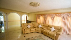 A spacious living room with a large beige sectional sofa, a decorative rug, and a large window with curtains. - Steel Love Villa (Montego Bay)