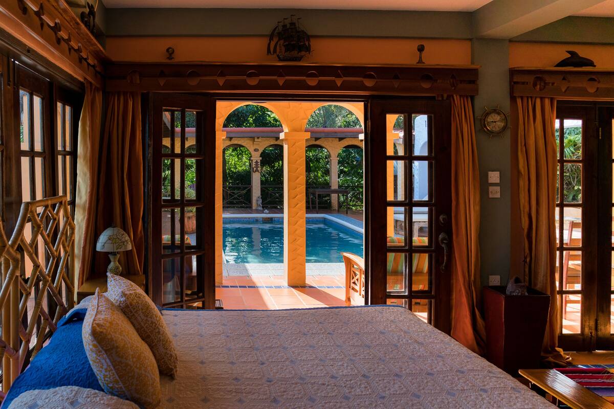Ein Schlafzimmer mit einem großen Bett und Blick auf einen Außenpool, sowie eine Holztür zum Poolbereich.