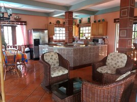 Una cocina con isla central, sillas de mimbre, una mesa de comedor y un refrigerador.