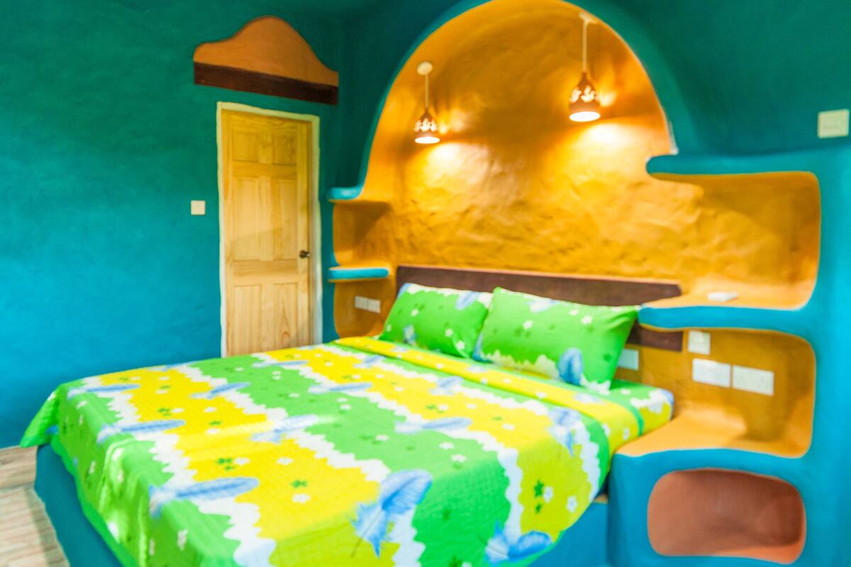 Ein einzigartig gestaltetes Schlafzimmer mit einem gewölbten Kopfteil, einer Holztür und einem Bett mit farbenfroher Bettdecke.
