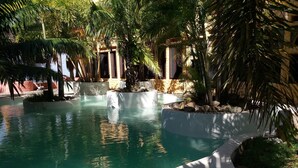 Un área de piscina con agua cristalina, rodeada de palmeras y un borde de piscina blanco.
