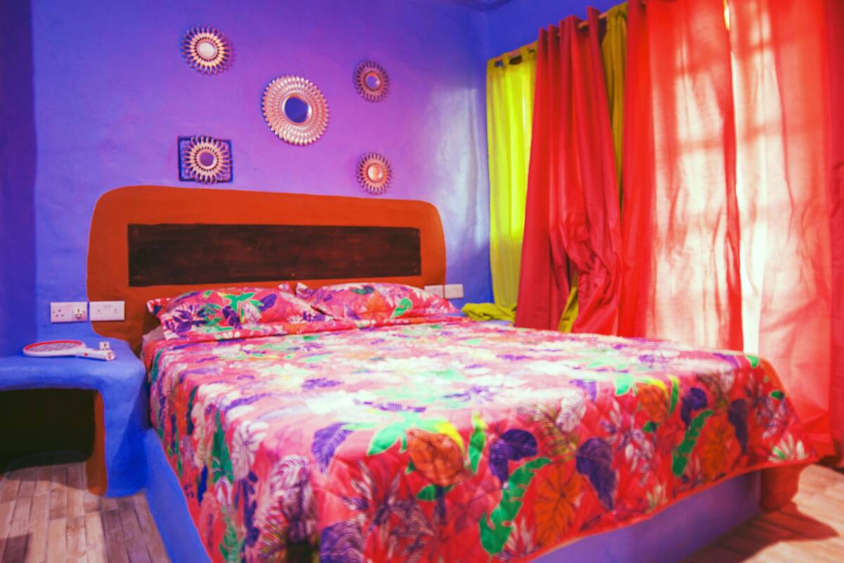 Ein Schlafzimmer mit einer farbenfrohen Bettdecke, einem blauen Nachttisch und einem roten Kopfteil.