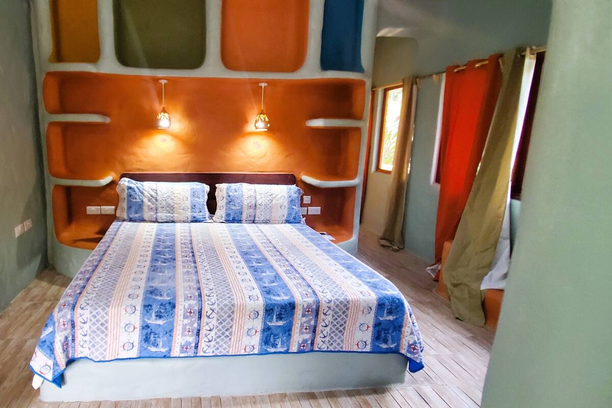 Ein kleines, gemütliches Schlafzimmer mit einem Bett, zwei Wandleuchten und einem mit Vorhängen drapierten Fenster.