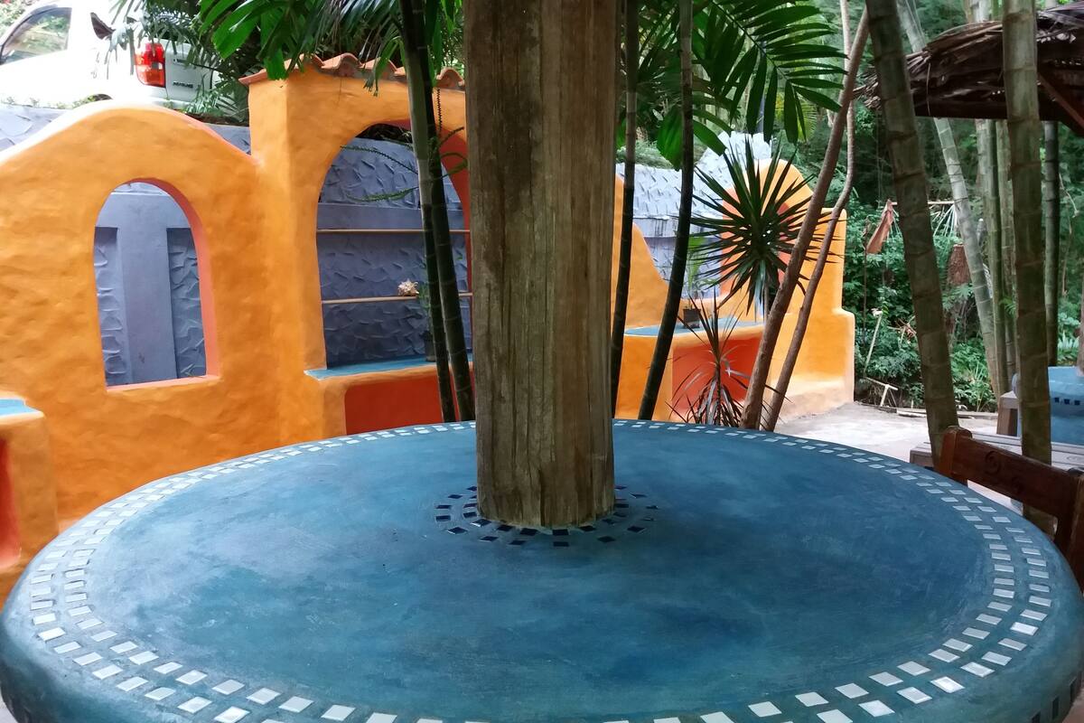 Ein blauer Tisch mit runder Form und dekorativer Kante, umgeben von einer lebhaften Wand in Orange und Blau mit Rundbogenfenstern.