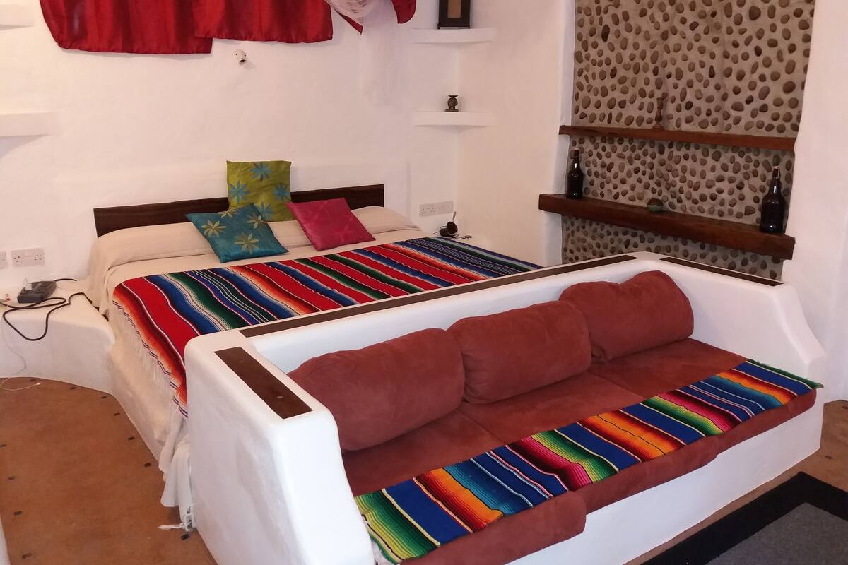 Ein Schlafzimmer mit einem Bett, einem roten Sofa, einer bunten Decke und einer Wand mit Muster.