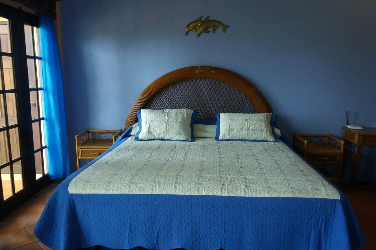 Ein Bett mit blauer und weißer Bettdecke, zwei Kissen, einem Holz-Kopfteil und einer Wanddekoration mit einem Delphin.