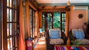 Un salón acogedor con muebles de mimbre, un ventanal con cortinas y vistas al exterior.