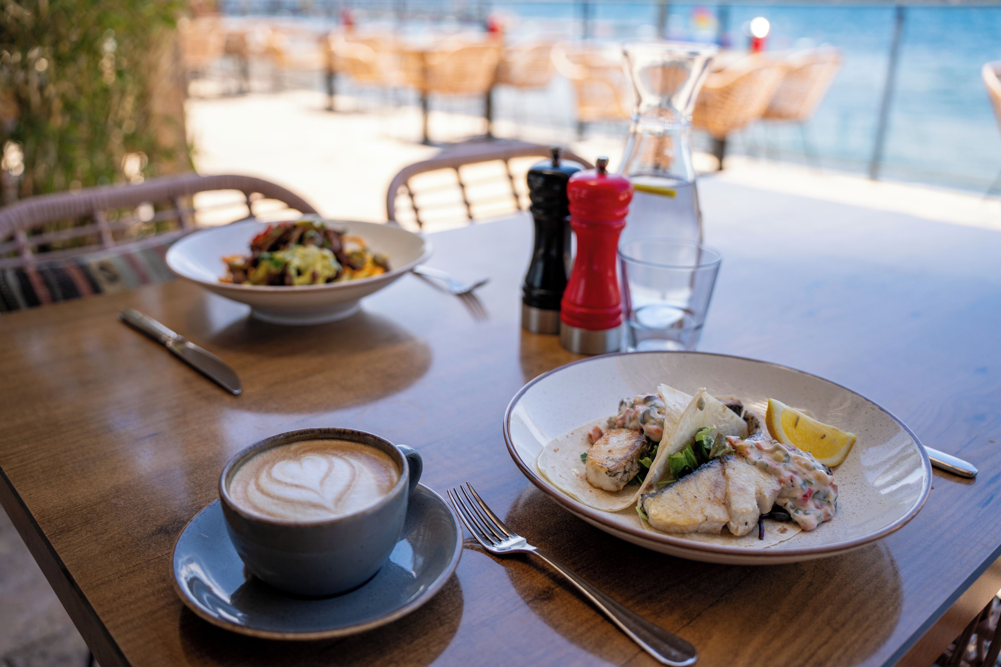 A dining table with a plate of food, a cup of coffee, and a glass of water.