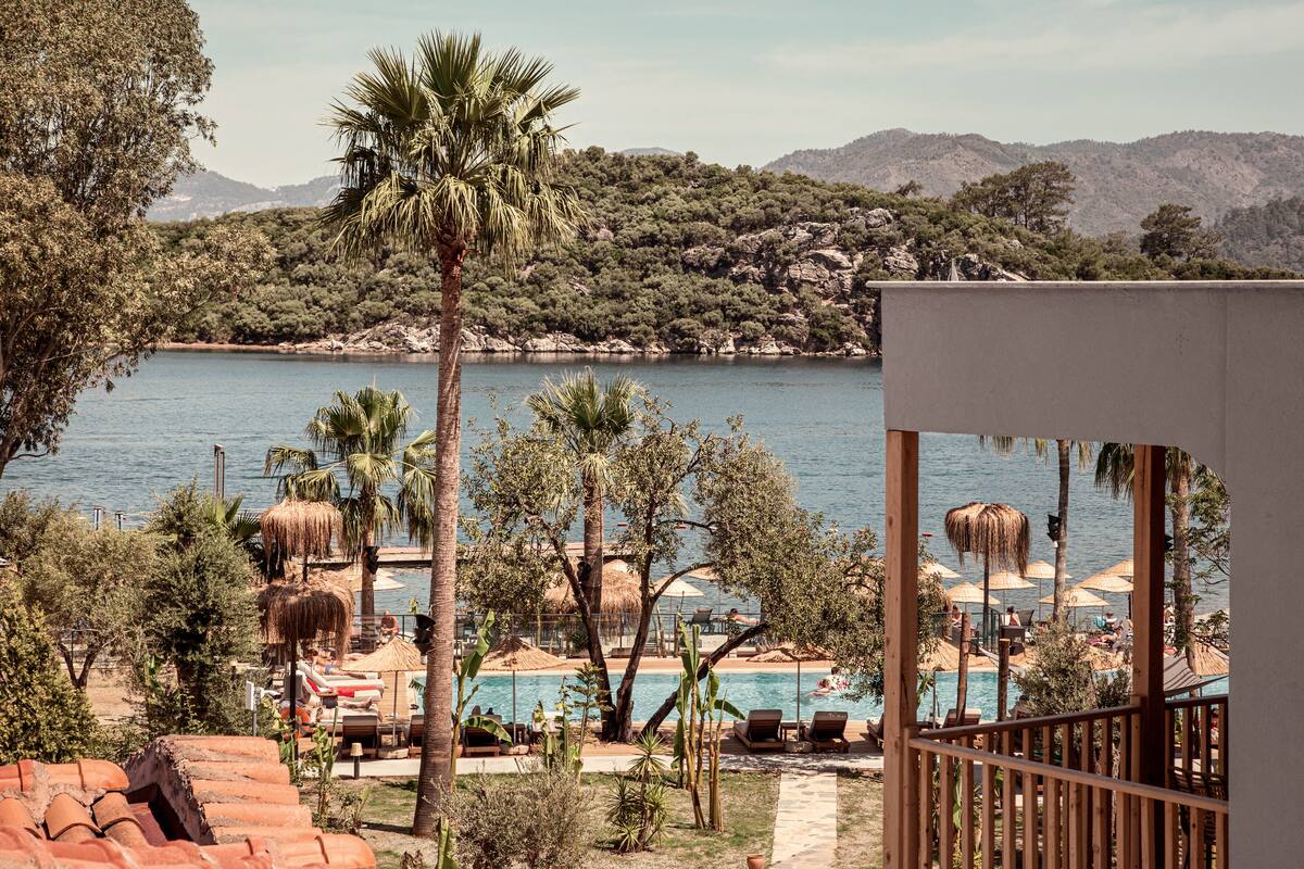 Un espace piscine agrémenté de chaises longues et de parasols, entouré d’arbres et offrant une vue sur la mer et les collines.