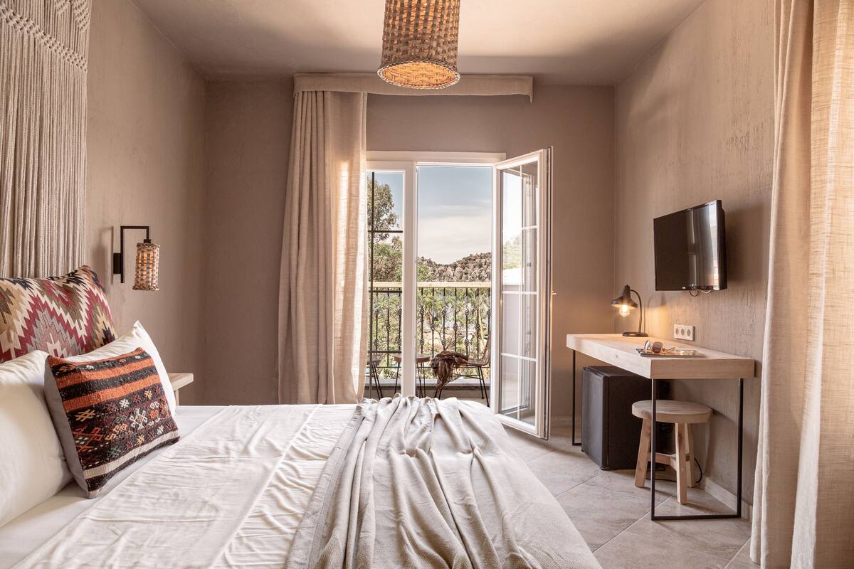 Une chambre avec un lit, un bureau, une chaise, une télévision et un balcon avec vue.