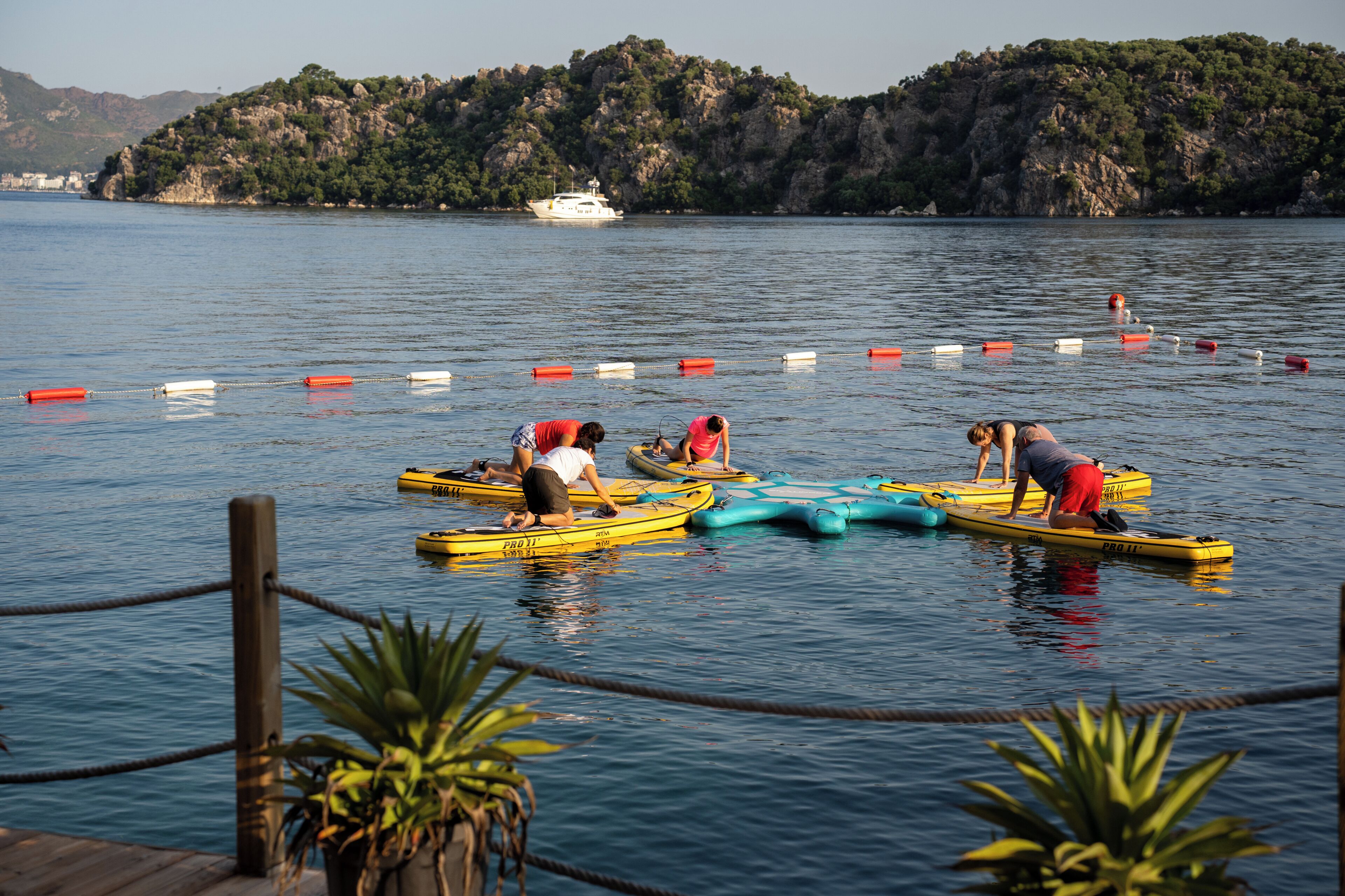 A calm lake with people on paddleboards, a wooden dock, and a boat in the background.