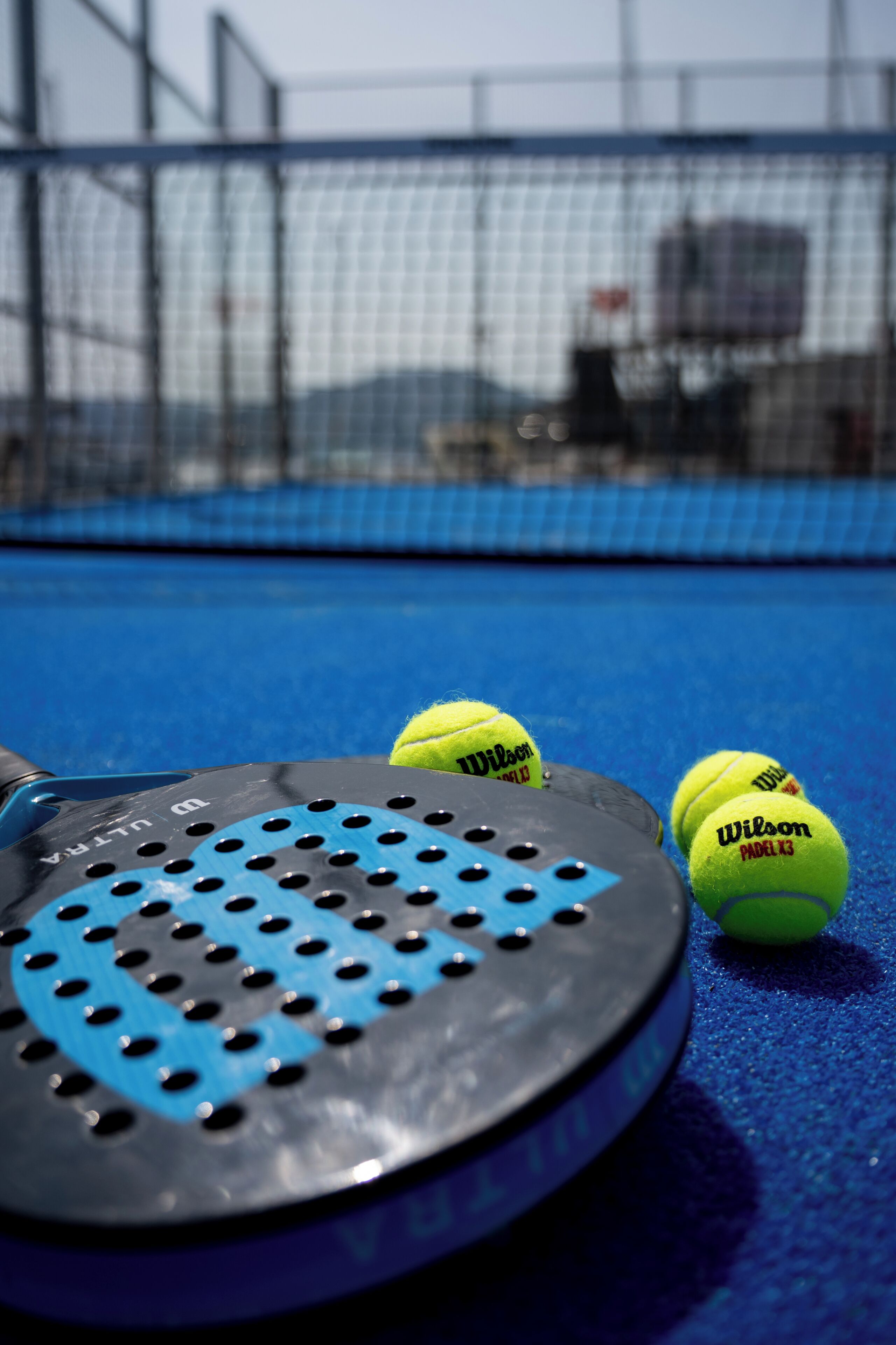A tennis racket and balls on a blue court with a net in the background.