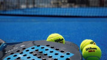 Una raqueta de tenis y pelotas en una cancha azul con una red al fondo.