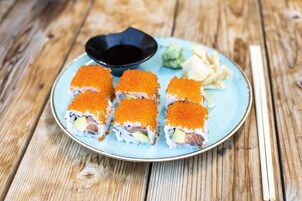 Un plato de sushi con huevas de pescado naranja, aguacate y un pequeño recipiente con salsa.