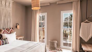 A bedroom with a bed, a hanging light fixture, a window with curtains, and a view of the outdoors.