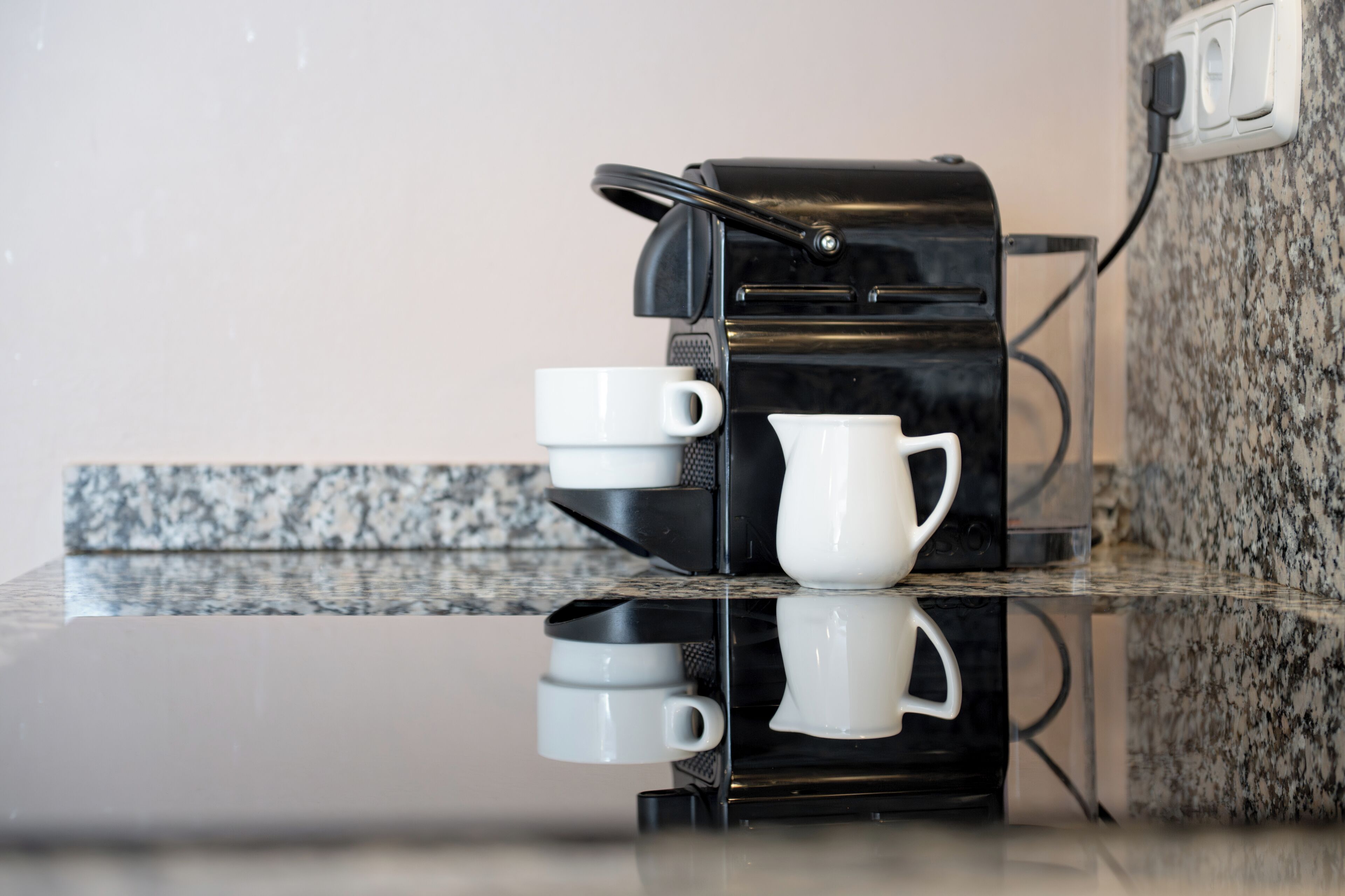 A coffee machine with a cup holder and a coffee pot on a granite countertop.