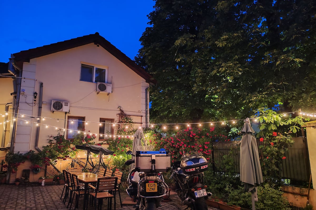 A patio area with a table and chairs, a motorcycle, and a house with string lights.