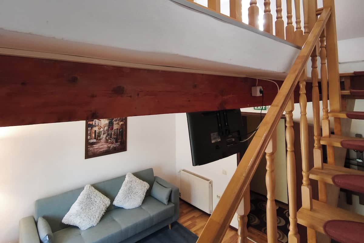 A wooden staircase with a handrail leading to an upper level. Below, a blue sofa with white cushions is positioned against a wall with a framed picture.