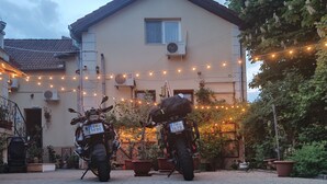 Two motorcycles parked in front of a building with string lights, potted plants, and a tiled pavement. - Pension Buon Gusto Sibiu - motorcycle friendly (Sibiu)