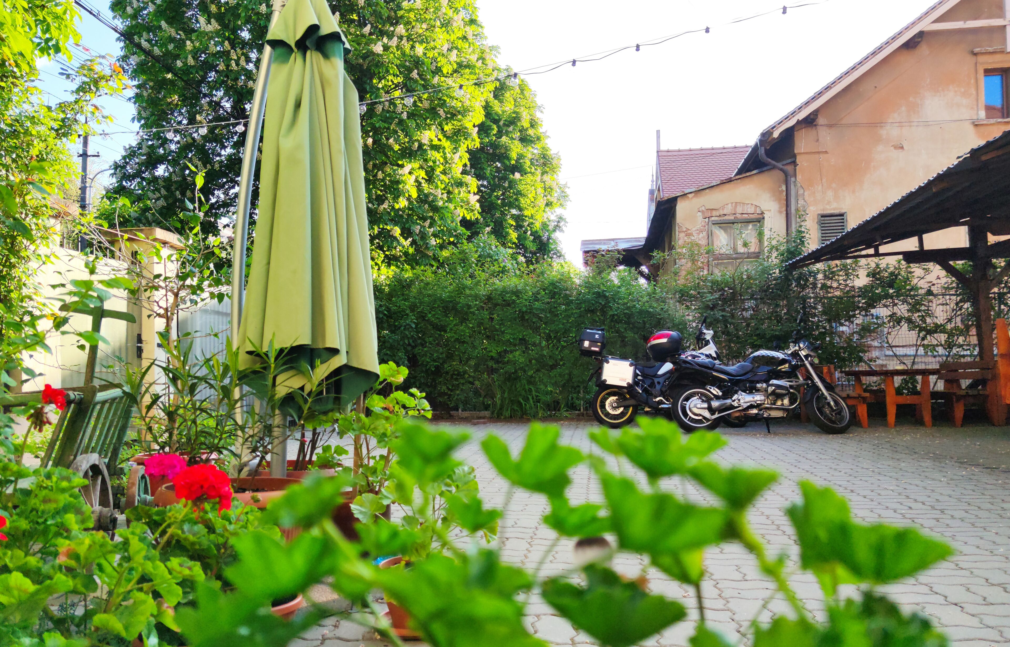 A garden with a motorcycle parked near a wooden table and a green umbrella.