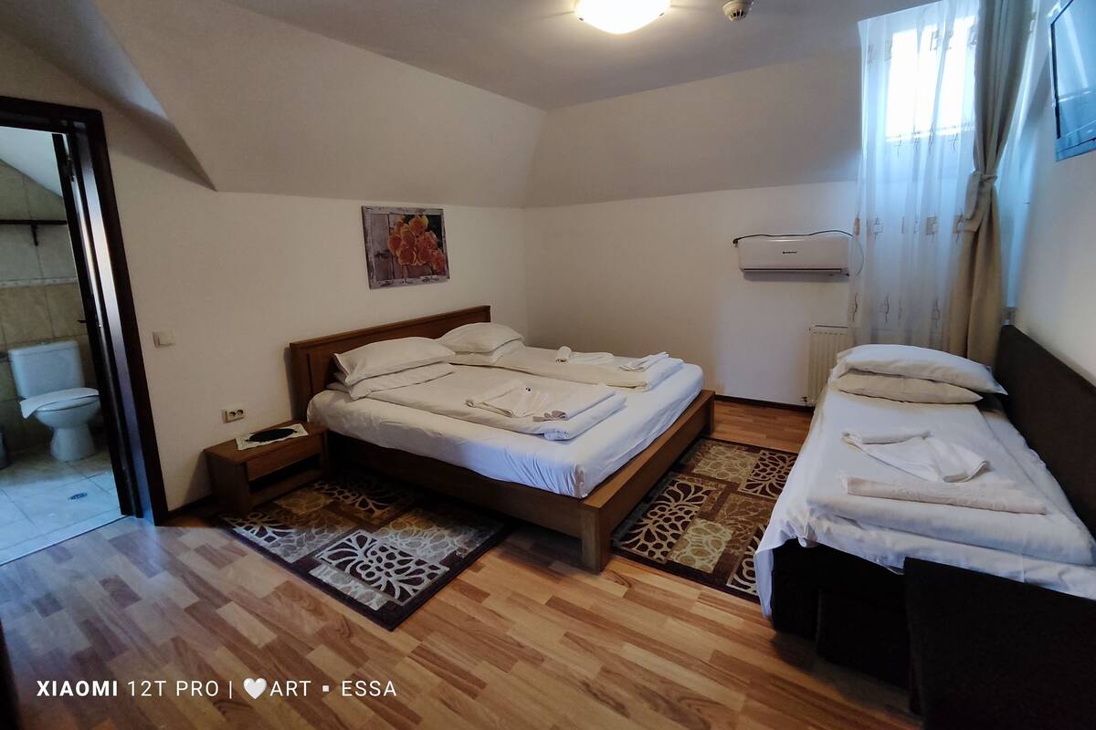 A bedroom with a wooden bed, a bedside table, a nightstand, a radiator, and a window with curtains.
