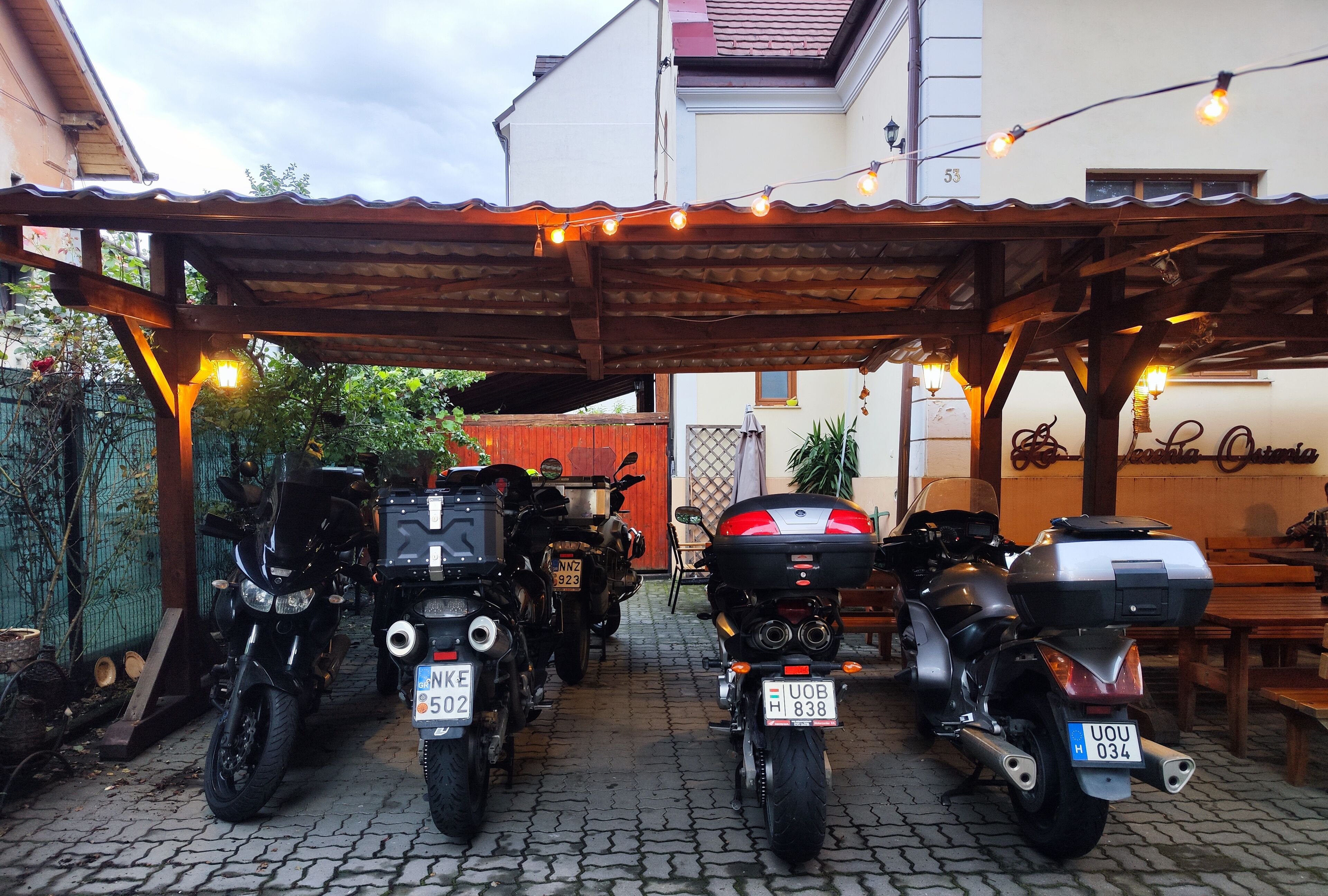 A covered outdoor area with motorcycles parked under a roof, a wooden bench, and a sign with a logo.