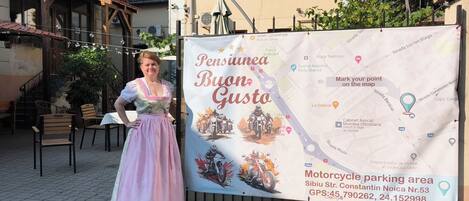 A woman in traditional attire standing in front of a map with a motorcycle parking area sign.
