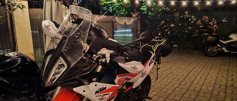 A motorcycle parked in a covered outdoor area with string lights and flowers in the background.