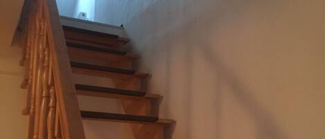 Un escalier en bois, doté d’une rampe, mène à un palier où se trouve une petite fenêtre.