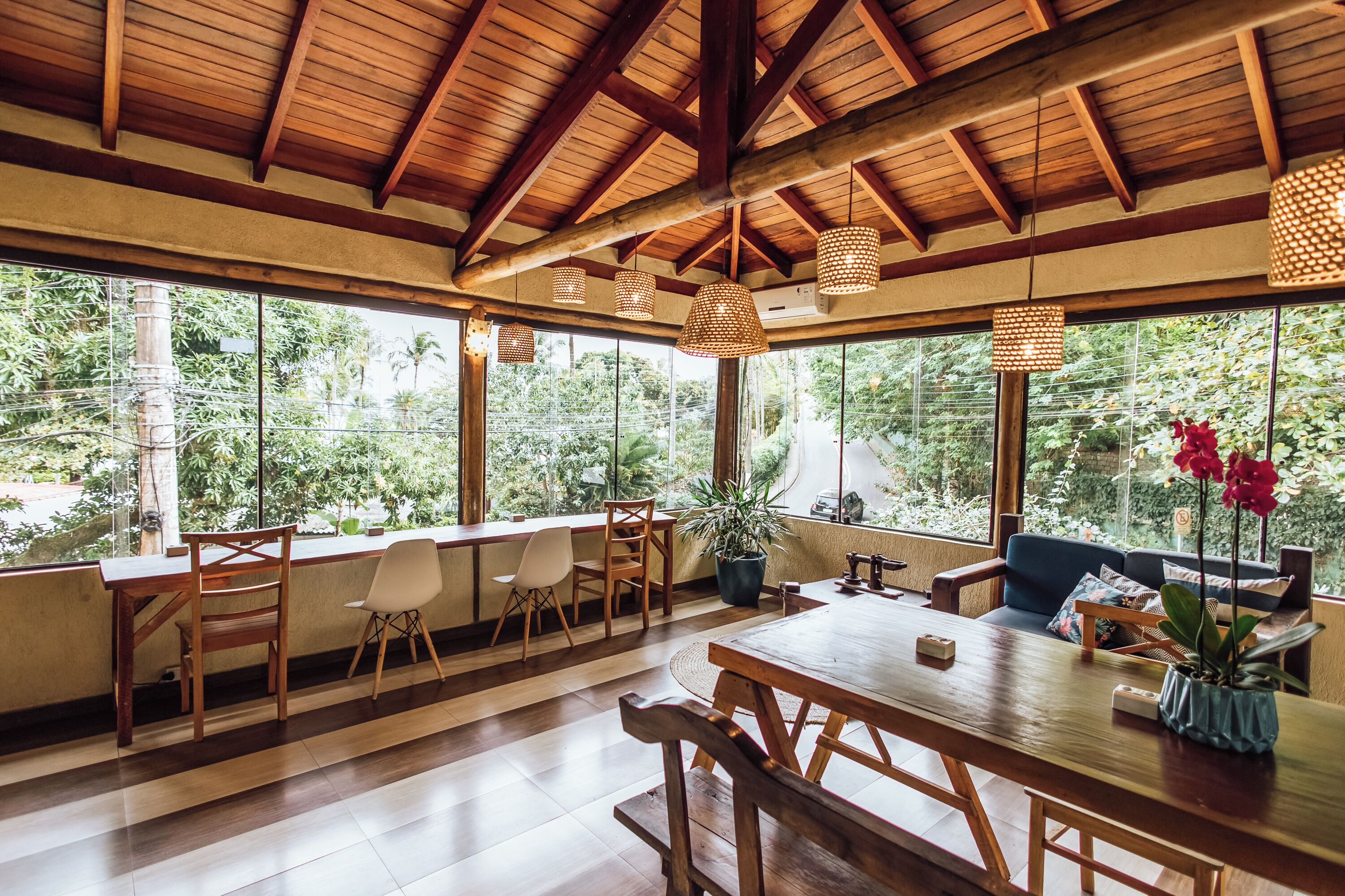 A spacious room with a wooden ceiling, large windows, and a dining area with wooden furniture.