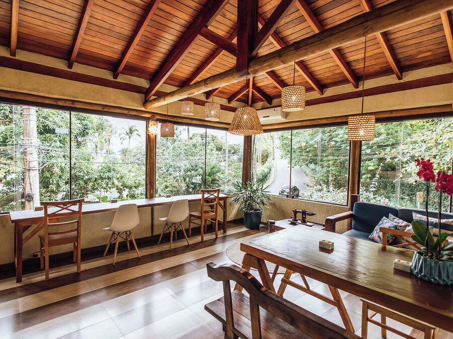 A spacious room with a wooden ceiling, large windows, and a dining area with wooden furniture.