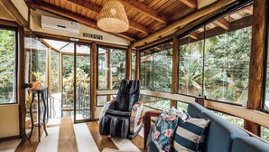 A room with a massage chair, a sofa with floral cushions, large windows, and a wooden ceiling. - Santa Smart Hotel (Ilhabela)