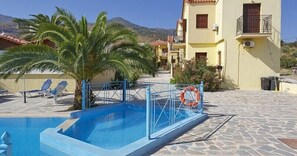 A swimming pool with a blue fence, palm trees, and a mountain in the background.