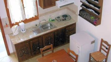 A compact kitchen with a sink, cabinets, a small refrigerator, and a dining table with chairs.