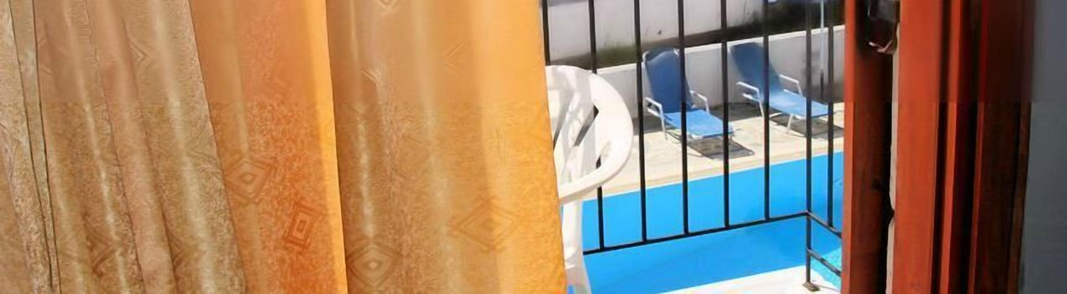 A balcony with a pool, blue chairs, and a white umbrella.