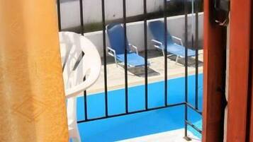 A balcony with a pool, blue chairs, and a white umbrella.