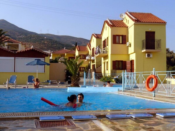 A swimming pool area with lounge chairs, a lifebuoy, and a building with balconies.