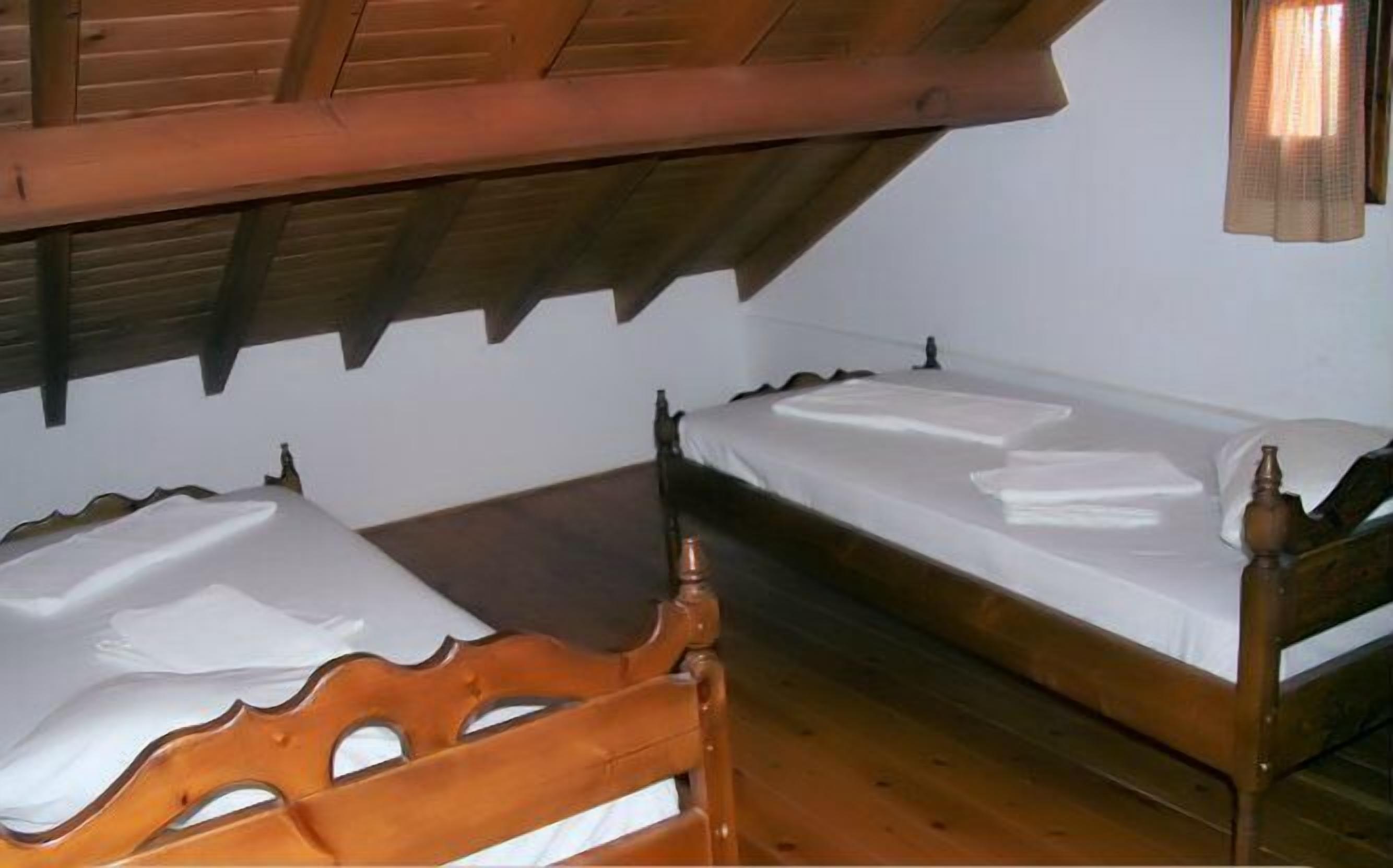 A small, single-room with two wooden beds and a sloped ceiling.