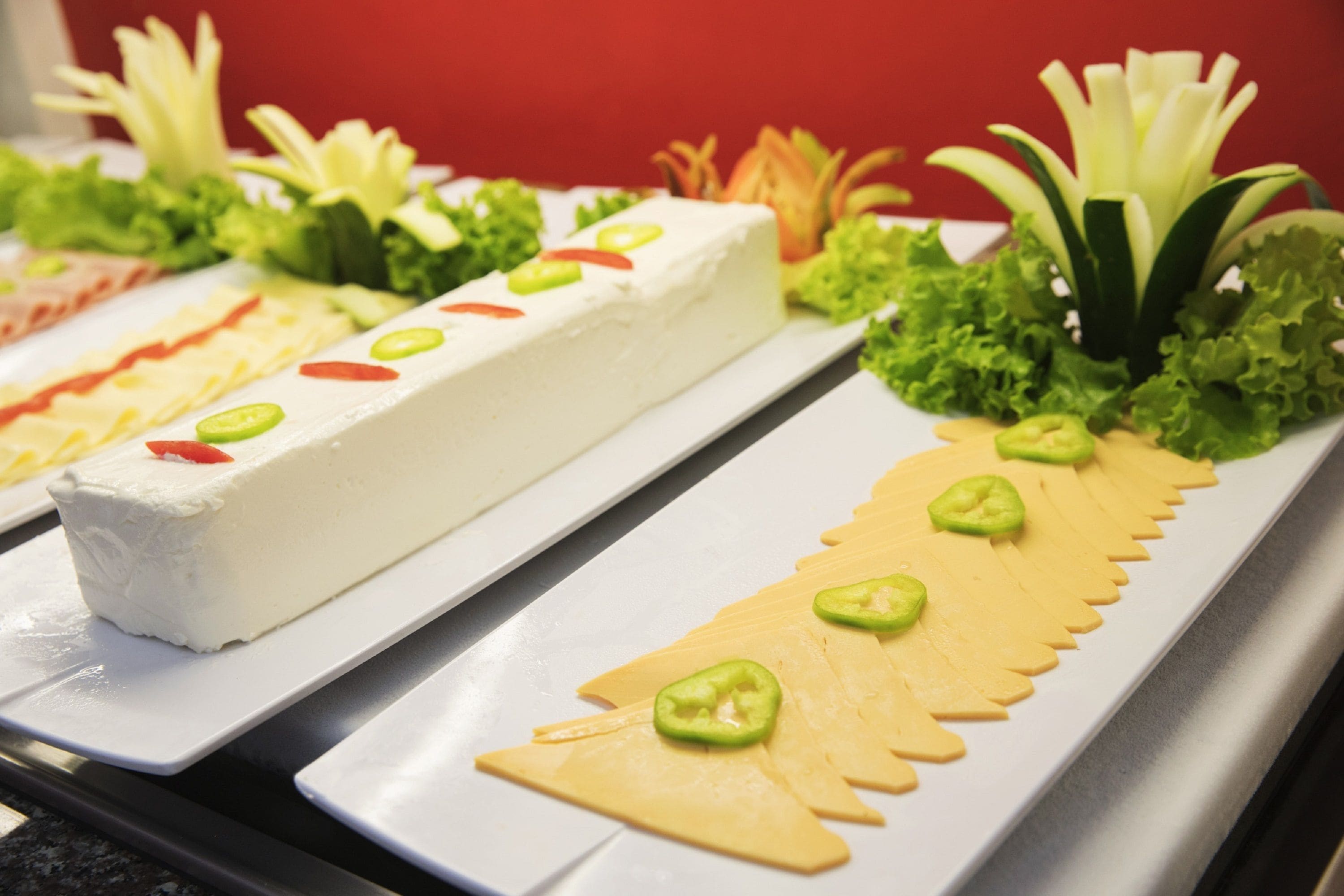 A buffet with various dishes including a large white block of food, green vegetable garnishes, and yellow pasta shapes.