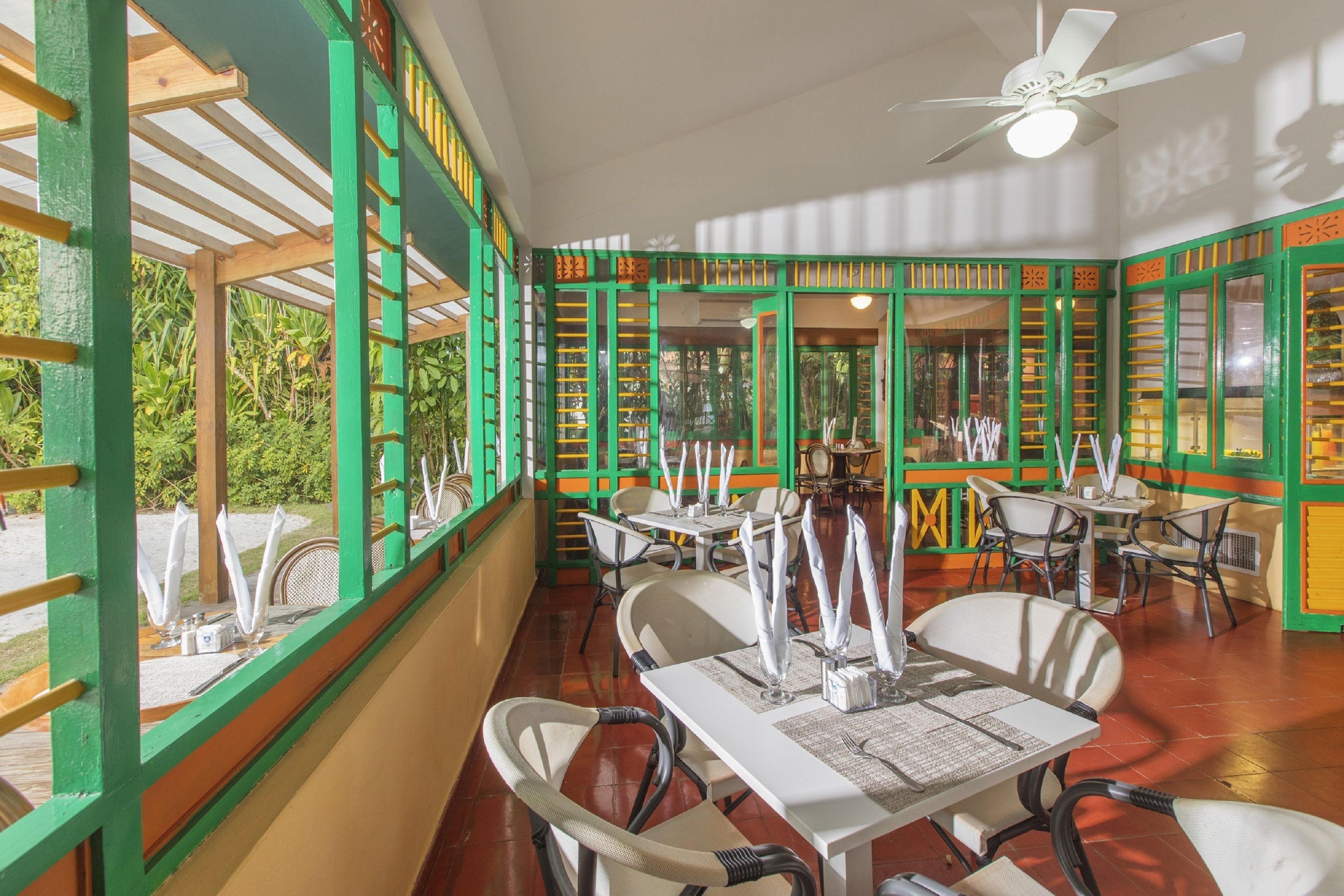 An indoor dining area with tables and chairs, a ceiling fan, and green-framed windows.