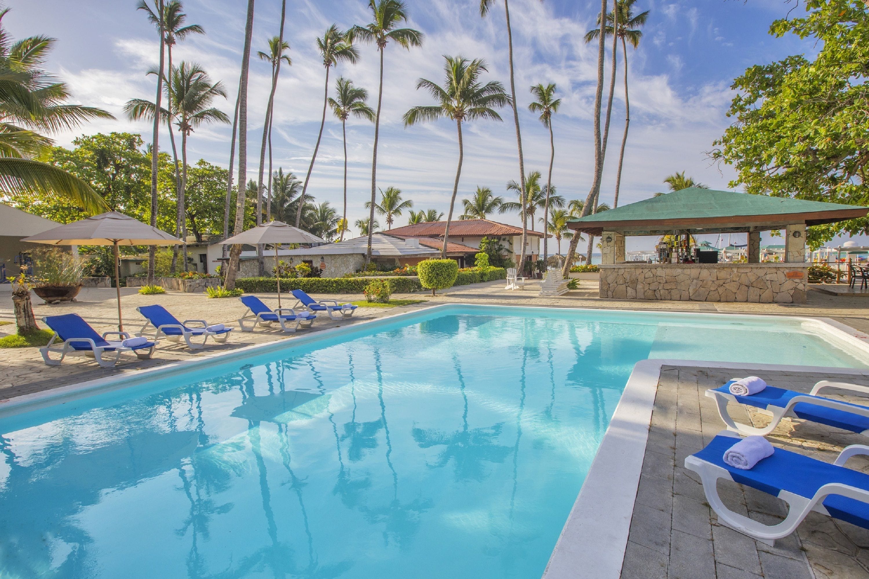 A swimming pool with lounge chairs, palm trees, and a gazebo.