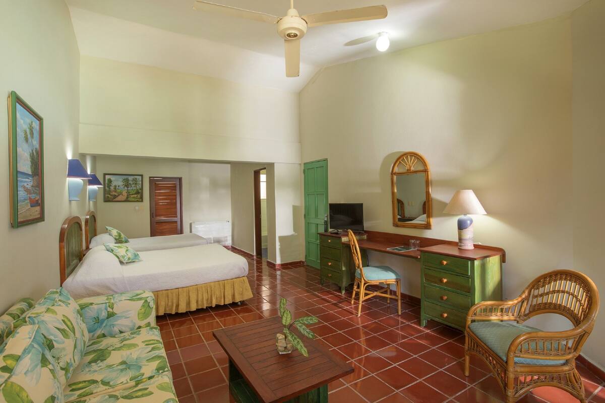 A hotel room with a bed, a desk, a chair, a dresser, and a ceiling fan.